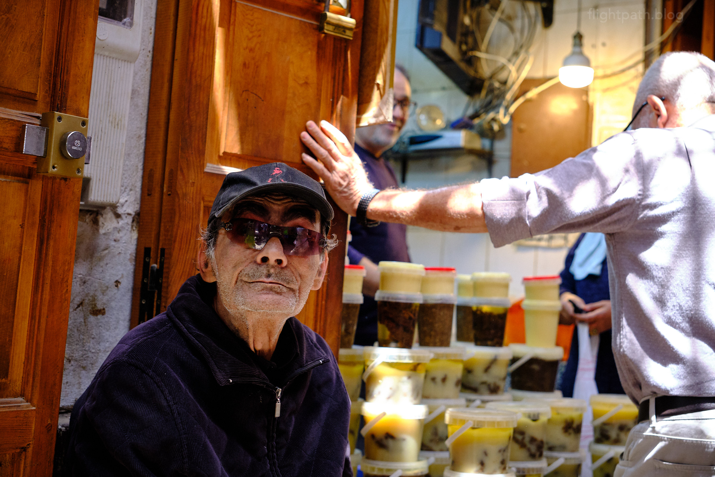 A man in a marketplace wearing a hat and sunglasses.